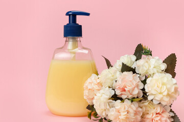 Obraz na płótnie Canvas Yellow liquid soap bottle and beautiful delicate flowers on a pink background. Clean hands concept. Shampoo, Liquid Soap, Aromatic Bath Salt And Other Toiletry.