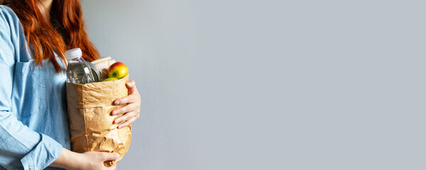 Woman holds paper bag of healthy food with copy space on gray background with copyspace