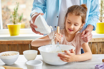 Father and daughter preparing dough together in kitchen
