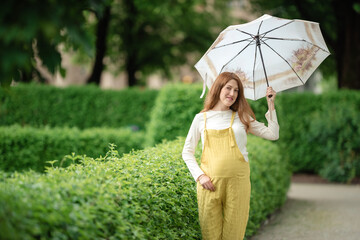 Young pregnant woman under umbrella in summer forest.