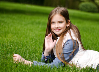 Portrait of adorable smiling little girl child preteen lying on grass in the park