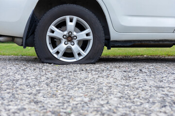 Close up of flat rear tire of white SUV track car vehicle automobile punctured by nail. Summer day, residential street. Selective focus, depth of field, space for copy.