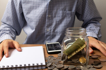 Saving money and investment concept. Coins in glass jar. Businessman holding coins putting in the glass. Financial and retirement planning concept for graphic design and poster