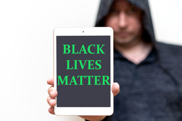 Portrait of a hooded white man holds tablet with the inscription Black Lives Matter. protests of racial discrimination.White studio wall.
