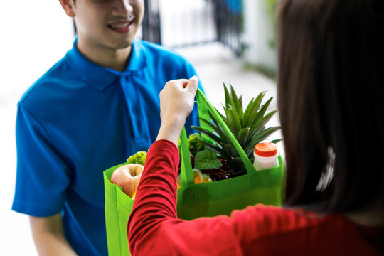 Asian delivery man delivering food, fruit, juice and vegetable to customer home - online grocery shopping service concept