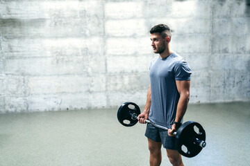 Fototapeta na wymiar Caucasian serious bodybuilder standing and holding barbell. In background wall.