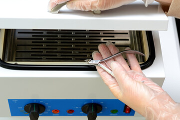 gloved hand with manicure forceps, preparing instruments for steam sterilization, disinfecting from...