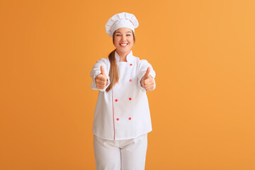 Young female chef showing thumb-up on color background