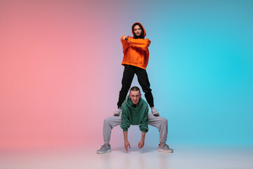 Boy and girl dancing hip-hop in stylish clothes on colorful gradient background at dance hall in neon. Youth culture, movement, style and fashion, action. Fashionable bright portrait. Street dance.