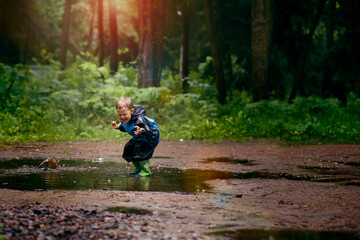 A little boy is jumping in a muddy puddle. Image with selective focus and toning