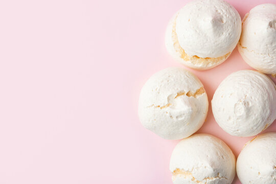 Home baked puffy meringue cookies on light pstel pink background. French Italian Swiss desserts. Baking poster template