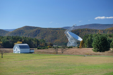 Large fully steerable telescope surrounded by trees and mountains points skyward. Blue sky. Science, astronomy, space research concept.