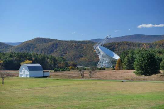 Large fully steerable telescope surrounded by trees and mountains points skyward. Blue sky. Science, astronomy, space research concept.