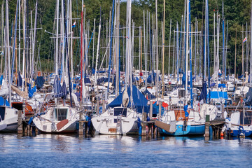 Many small sailing boats with masts without rigging anchor at a landing stage in the harbour of the big lake