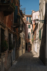 Fototapeta na wymiar One woman is walking along the narrow and bright street of sunny Venice, Italy.