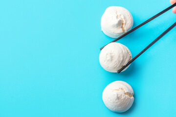 Woman holding black chop sticks in hand picking up home baked meringue cookies on blue background