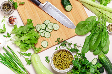 Stainless steel kitchen vegetable knife lies on a wooden cutting board surrounded by vegetables and herbs. Cooking ingredients  top view. Green salad ingredients  - spinach, lettuce, parsley, cucumber