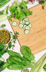 Cooking ingredients and a cutting board on a light background, top view, free space for text. Salad ingredients - spinach, lettuce, cucumbers, parsley flat lay. Food background. Diet and vegan food