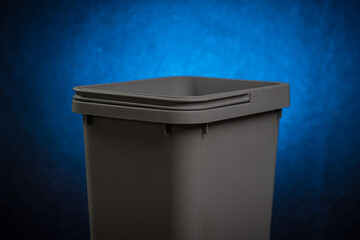 A gray plastic trash can with open top and visible handle on a dissolving blue background in...