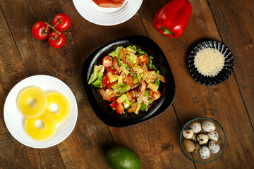 Pan-Asian salad with in a black plate and a row of ingredients on a wooden table.