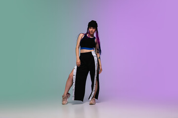 Beautiful sportive girl dancing hip-hop in stylish clothes on colorful gradient background at dance hall in neon light. Youth culture, movement, style and fashion, action. Fashionable bright portrait.