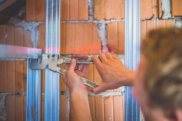 Drywall plaster stud crimpers in action. A person holding and using stud crimping tool in hand while building a metal drywall construction in a house during renovation
