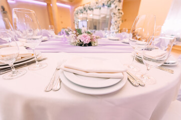 Banquet, restaurant. Table setting with tablecloth. White plates, cutlery, glasses, napkin, floral arrangements, food, chairs, flowers