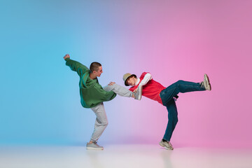 In action. Sportive boys dancing hip-hop in stylish clothes on colorful gradient background at...