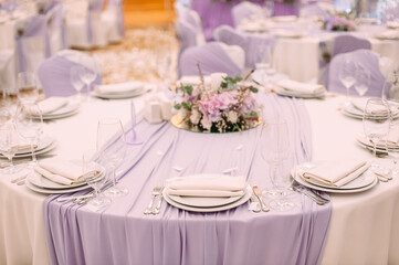 Banquet, restaurant. Table setting with tablecloth. White plates, cutlery, glasses, napkin, floral arrangements, food, chairs, flowers