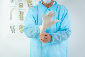 Doctor wearing single use blue gown puts on white latex gloves to prevent coronavirus spreading