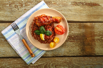 Chicken legs with red rice in tomato-garlic sauce on a plate on a wooden