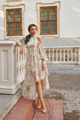Full-body portrait of young woman wearing elegant chiffon floral dress standing at street and...