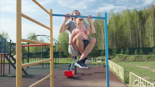 Family work out. Young man does pull ups with his baby. Adult male performs work out with his little child as additional weight.