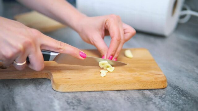 Woman cutting garlic with a knife on a wooden board. High quality 4k footage. She has bright manicure, pink and orange nails. 