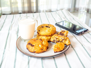 Chunky chewy chocolate chip soft cookies with cup of cold milk for breakfast, selective focus on cookie. With a mobile phone on table.