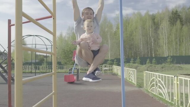 Family work out. Young man does pull ups with his baby. Adult male performs work out with his little child as additional weight. Flat log profile without color grading