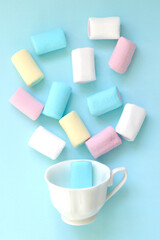 Salute of colorful pastel marshmallow souffle from a small white coffee Cup on a blue background . Selective focus. Celebration and fun. Sweets