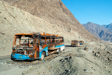 The frame of the burnt bus on the mountain road in Pakistan. Few buses in the valley. Dangerous touristic landscape. Terrorism accident during the travelling