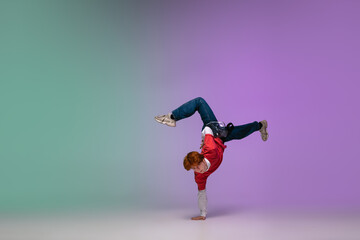 Beautiful sportive boy dancing hip-hop in stylish clothes on colorful gradient background at dance...