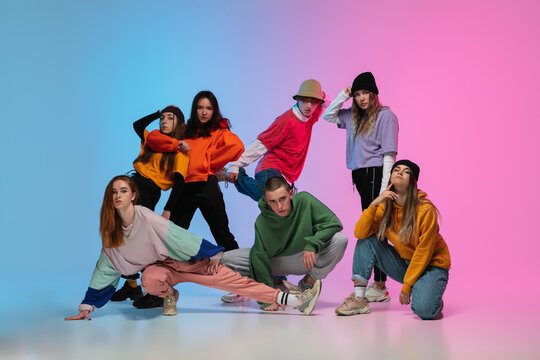 Group of dancers, boys and girls dancing hip-hop in stylish clothes on colorful gradient background at dance hall in neon. Youth culture, movement, style and fashion, action. Fashionable portrait.