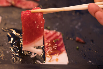 Hands holding chopsticks and row of variety beaf sliced in plate.Fresh meat for cooking...