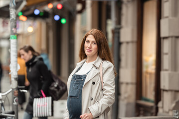 Beautiful young pregnant woman wearing casual clothes walking through the city streets. concept of motherhood and pregnancy. street portrait among cars close up view.