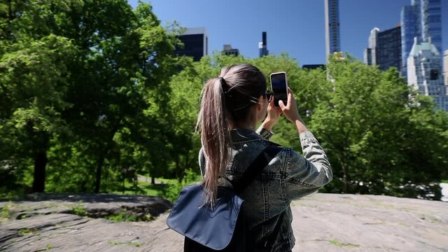A young woman taking a photo of the Manhattan Skyline from the Central Park