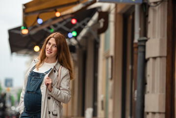 Beautiful young pregnant woman wearing casual clothes walking through the city streets. concept of motherhood and pregnancy. street portrait among cars close up view.