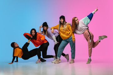 Group of dancers, boys and girls dancing hip-hop in stylish clothes on colorful gradient background at dance hall in neon. Youth culture, movement, style and fashion, action. Fashionable portrait.
