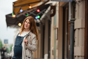 Beautiful young pregnant woman wearing casual clothes walking through the city streets. concept of motherhood and pregnancy. street portrait among cars close up view.