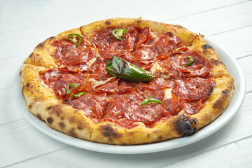 Appetizing homemade pizza with chorizo salami, hot pepper and melted cheese on a white plate on a white wooden background