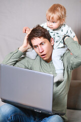 young man working at home with a laptop with a baby on his hands. Stay home concept. Home office with kids.