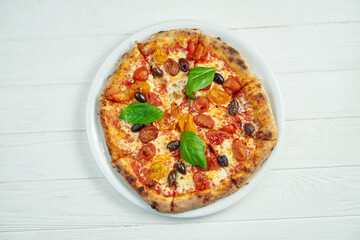 Appetizing, homemade pizza with margarita with cherry tomatoes, basil and mozzarella on a white plate on a white wooden background