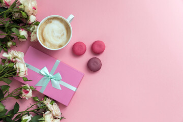 Flatlay pink coral background, the cup of cappuccino coffee and sweets macaroons, spring white roses, giftbox, beauty stuff - hair pin, nail polish and parfum. Best gift for woman